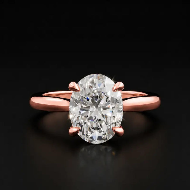 Front view of a 1.5 carat oval cut diamond solitaire engagement ring in an 18kt rose gold 4 claw setting by TJ Diamond