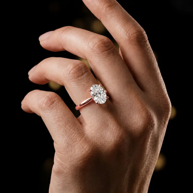 1.5 carat oval cut diamond solitaire engagement ring in an 18kt rose gold 4 claw setting worn on a hand, by TJ Diamond