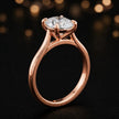 Angled side view of a 1.5 carat oval cut diamond solitaire engagement ring in an 18kt rose gold 4 claw setting by TJ Diamond