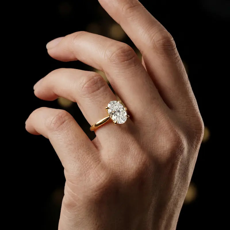 1.5 carat oval cut diamond solitaire engagement ring in an 18kt yellow gold 4 claw setting worn on a hand, by TJ Diamond