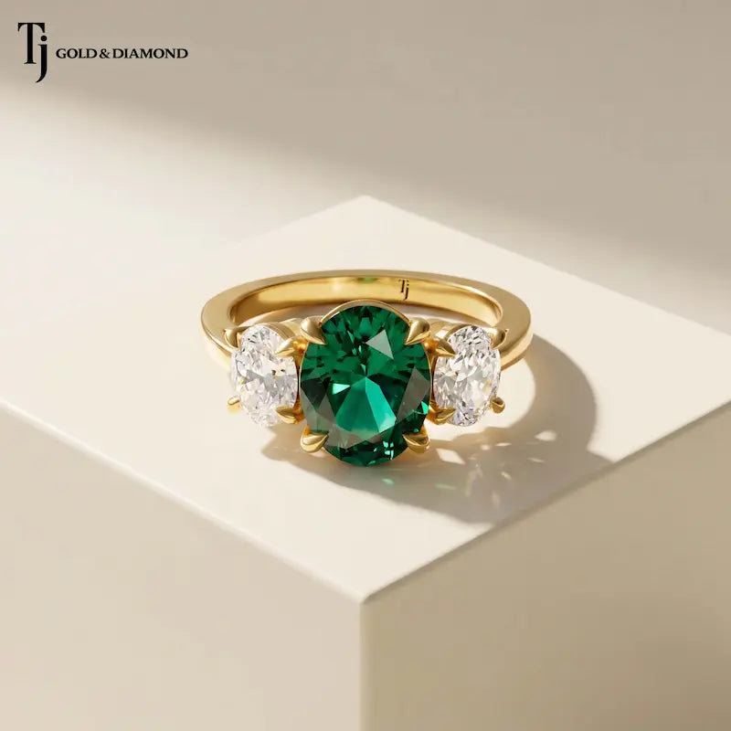 Front view of an oval lab-created emerald and diamond trilogy engagement ring in 18kt yellow gold.