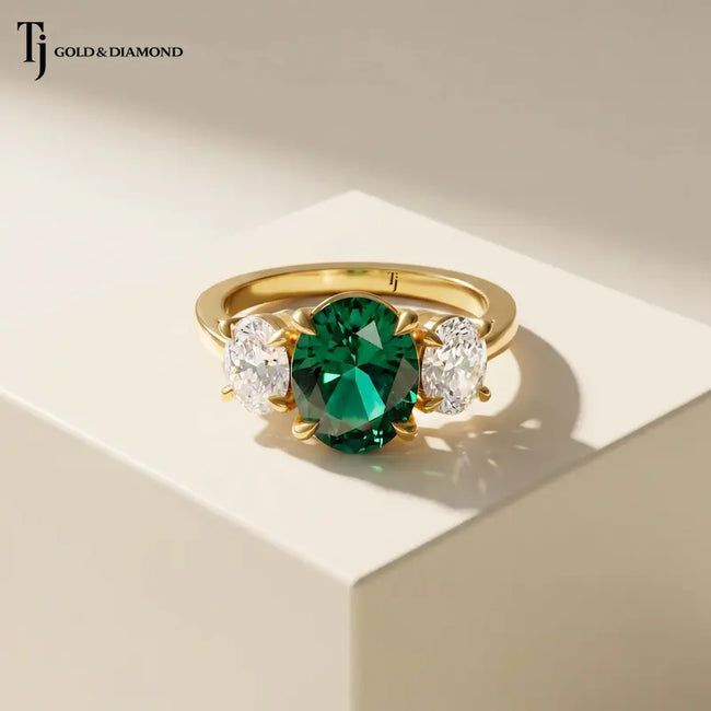 Front view of an oval lab-created emerald and diamond trilogy engagement ring in 18kt yellow gold.