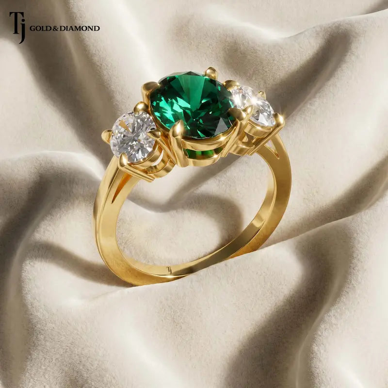 Close Up view of an oval lab-created emerald and diamond trilogy engagement ring in 18kt yellow gold.