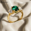Close Up view of an oval lab-created emerald and diamond trilogy engagement ring in 18kt yellow gold.