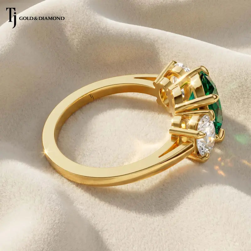 Side View of an oval lab-created emerald trilogy engagement ring in 18kt yellow gold with oval lab-grown diamond side stones and an open basket setting.