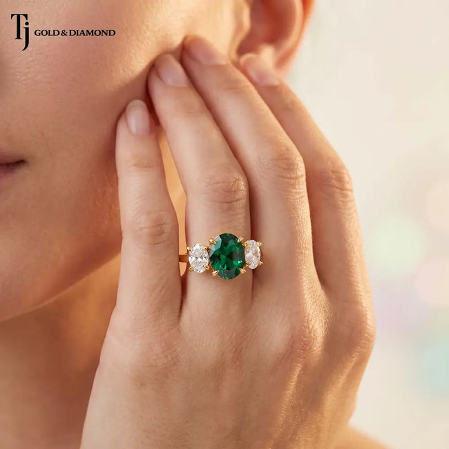 Hand wearing an oval lab-created emerald trilogy engagement ring in 18kt yellow gold with oval lab-grown diamond side stones.