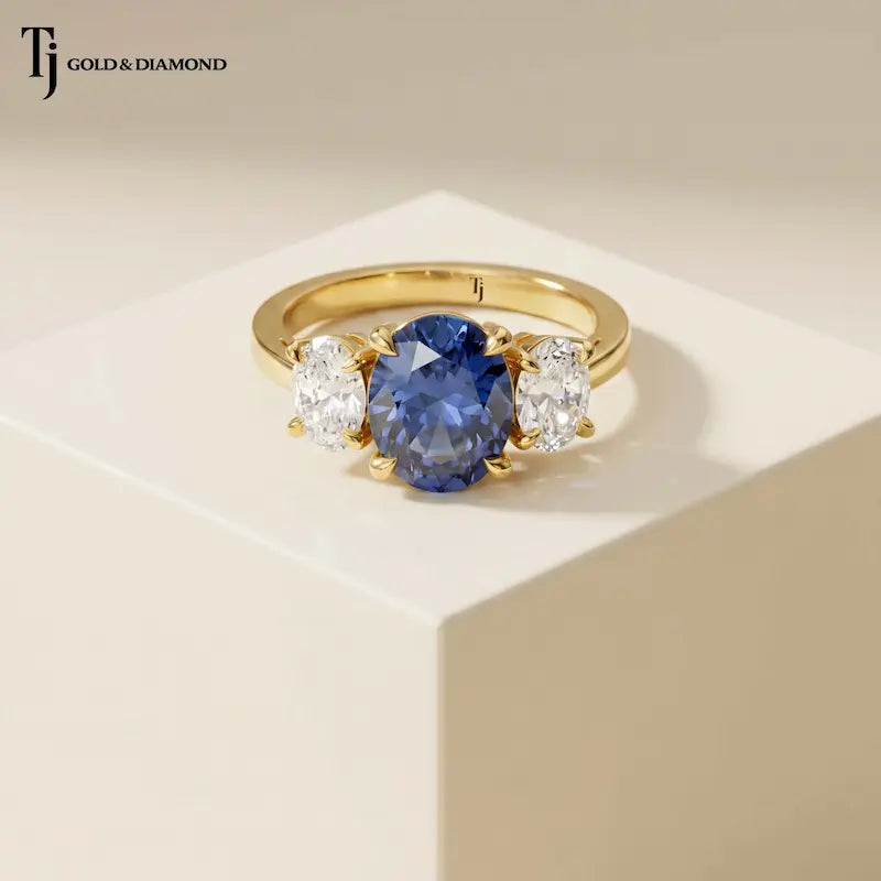 Oval Cut Lab-Created Blue Sapphire & Lab-Grown Diamond Trilogy Ring in 18kt yellow gold featuring an oval royal blue sapphire with oval lab-grown diamond side stones.