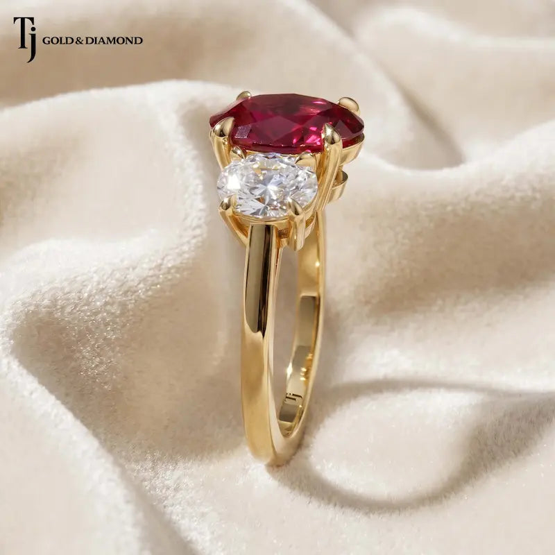 Side profile of an oval cut lab-created ruby trilogy engagement ring in 18kt yellow gold with oval lab-grown diamond side stones and a four claw basket setting.