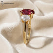Side profile of an oval cut lab-created ruby trilogy engagement ring in 18kt yellow gold with oval lab-grown diamond side stones and a four claw basket setting.