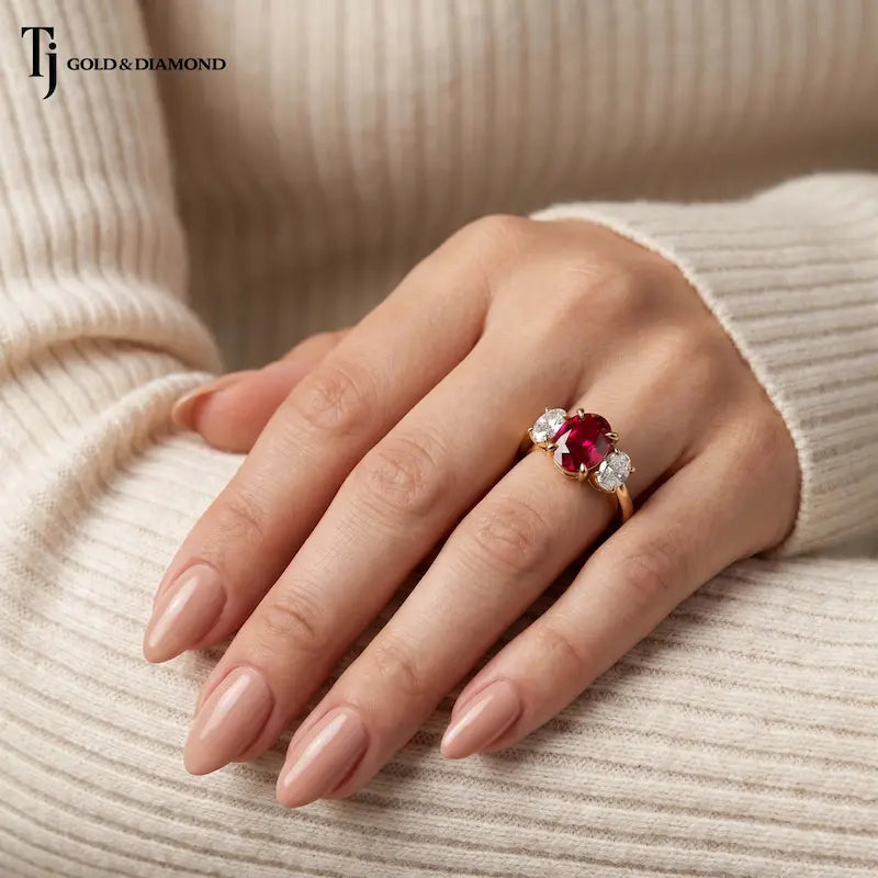 Model wearing an oval cut lab-created ruby trilogy engagement ring in 18kt yellow gold with oval lab-grown diamond side stones.