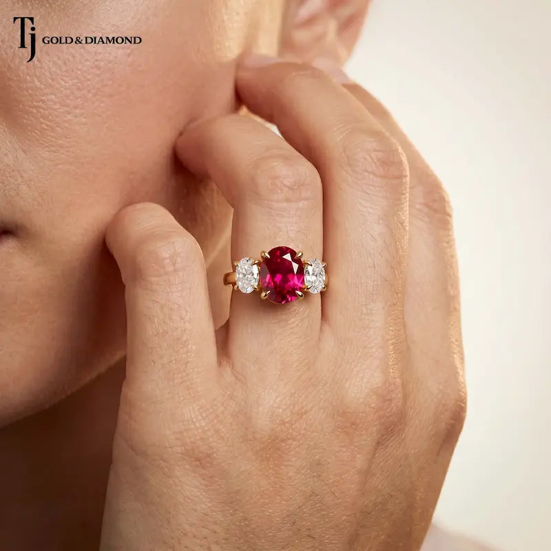 Model wearing an oval cut lab-created ruby trilogy engagement ring in 18kt yellow gold with oval lab-grown diamond side stones.