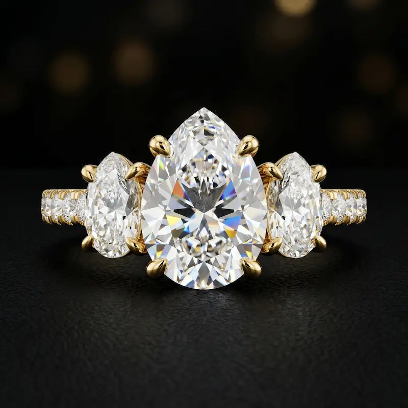 Front view of a pear cut three-stone lab-grown diamond engagement ring in 18kt yellow gold with diamond shoulders