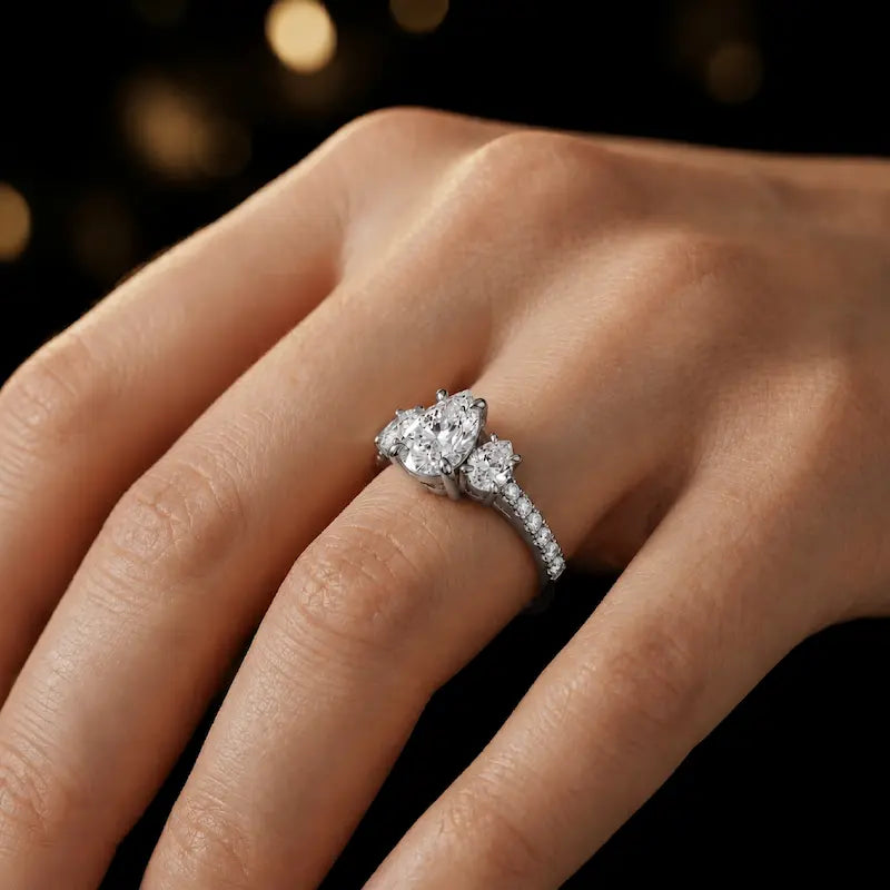 Pear cut three-stone lab-grown diamond engagement ring in 18kt white gold with diamond shoulders worn on hand