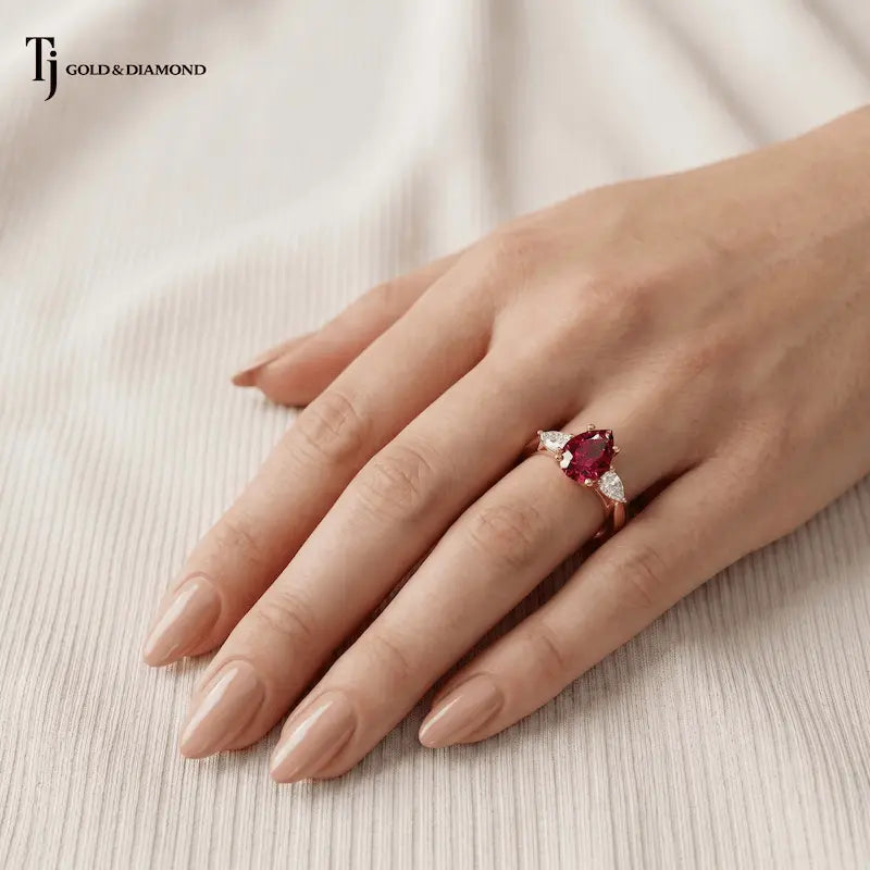 Hand wearing a pear cut lab-created ruby trilogy engagement ring in 18kt yellow gold with pear cut lab-grown diamond side stones.