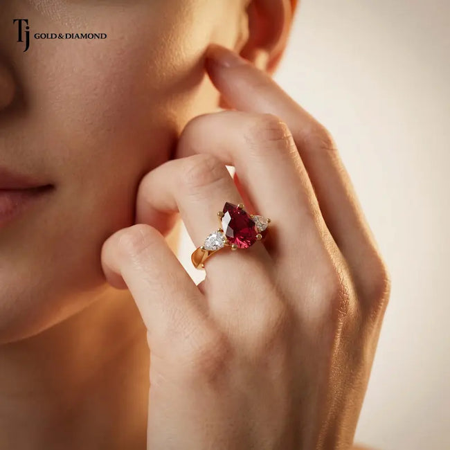 Model wearing a pear cut lab-created ruby trilogy engagement ring in 18kt yellow gold with pear cut lab-grown diamond side stones.