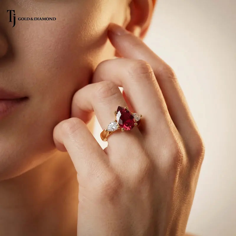 Model wearing a pear cut lab-created ruby trilogy engagement ring in 18kt yellow gold with pear cut lab-grown diamond side stones.