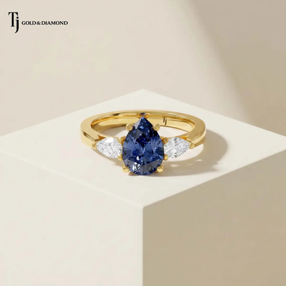 Pear Cut Lab-Created Blue Sapphire & Lab-Grown Diamond Trilogy Ring in 18kt yellow gold with a pear-shaped royal blue sapphire and pear-shaped lab-grown diamond trilogy setting.
