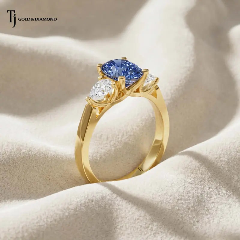 Side angle of a Pear Cut Lab-Created Blue Sapphire & Lab-Grown Diamond Trilogy Ring in 18kt yellow gold highlighting the elevated basket setting and pear-shaped gemstones.