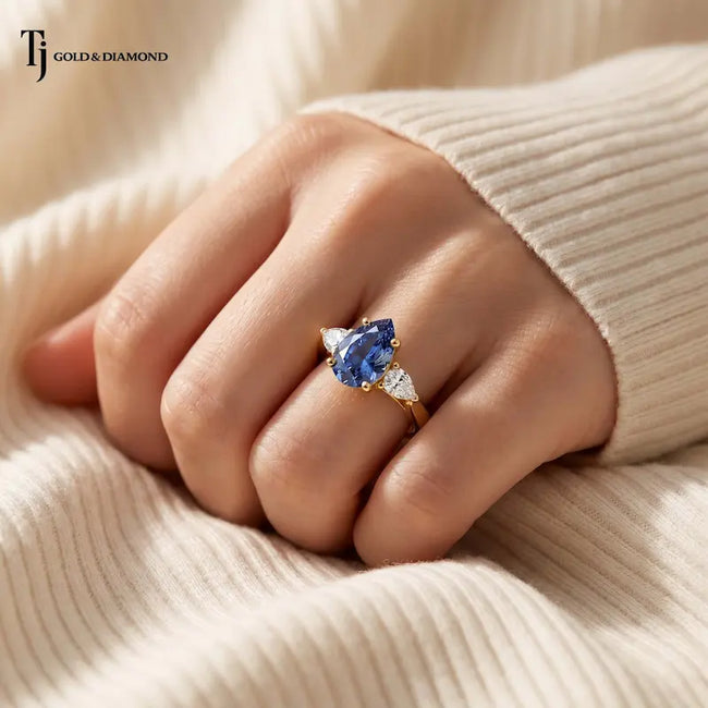 Pear Cut Lab-Created Blue Sapphire & Lab-Grown Diamond Trilogy Ring in 18kt yellow gold worn on hand showcasing its elegant pear-shaped trilogy design.