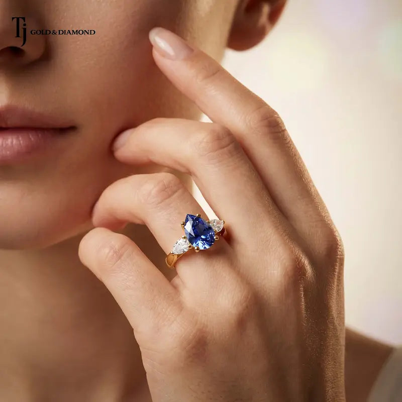 Model wearing a Pear Cut Lab-Created Blue Sapphire & Lab-Grown Diamond Trilogy Ring in 18kt yellow gold with pear-shaped lab-grown diamond side stones.