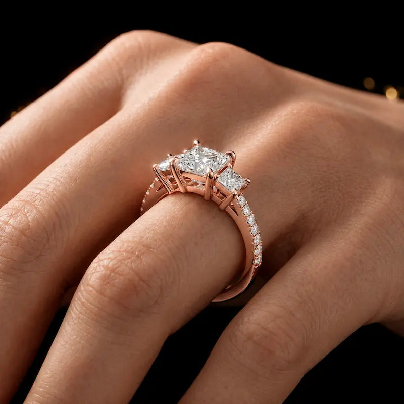Princess cut three-stone lab-grown diamond engagement ring in 18kt rose gold with diamond shoulders worn on hand