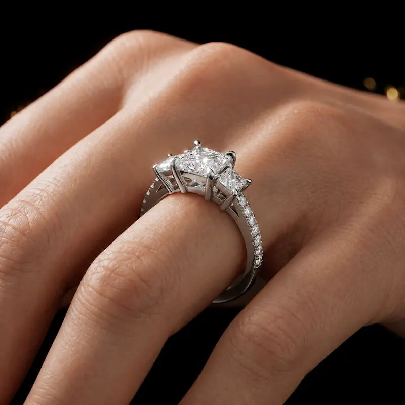 Princess cut three-stone lab-grown diamond engagement ring in 18kt white gold with diamond shoulders worn on hand