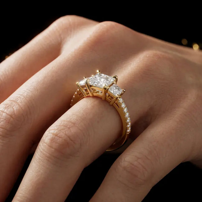 Princess cut three-stone lab-grown diamond engagement ring in 18kt yellow gold with diamond shoulders worn on hand