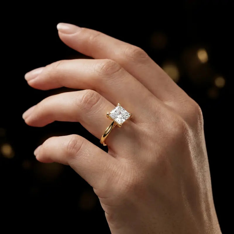 1.5 carat princess cut diamond solitaire engagement ring in an 18kt yellow gold 4 claw setting worn on a hand, by TJ Diamond