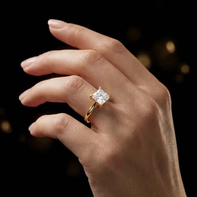 1.5 carat princess cut diamond solitaire engagement ring in an 18kt yellow gold 4 claw setting worn on a hand, by TJ Diamond