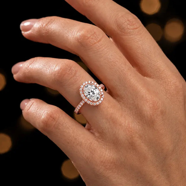 Oval cut halo lab-grown diamond engagement ring worn on hand in 18kt rose gold.