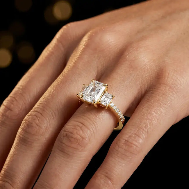 Radiant cut three-stone lab-grown diamond engagement ring in 18kt yellow gold with diamond shoulders worn on hand
