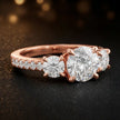 Side view of a round cut three-stone lab-grown diamond engagement ring in 18kt rose gold with diamond shoulders