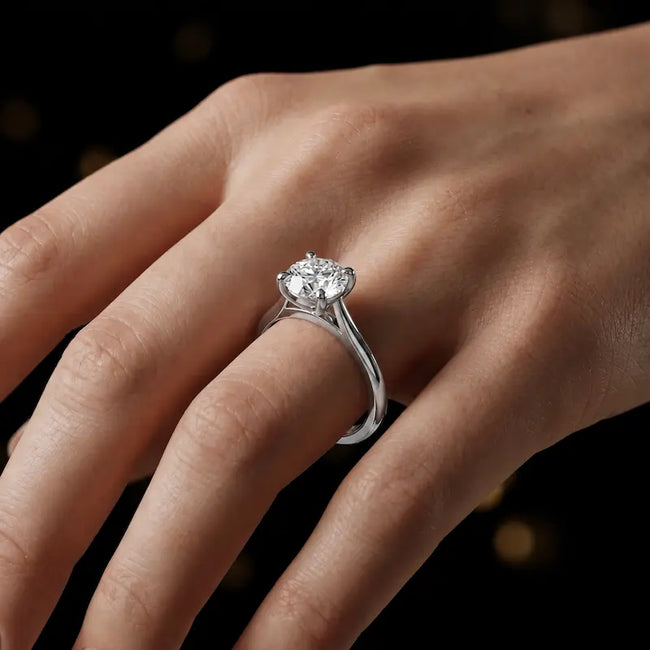 Round brilliant cut diamond solitaire engagement ring in an 18kt white gold 4 claw setting worn on a hand, by TJ Diamond