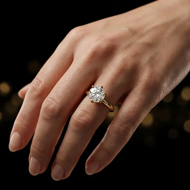 1.5 carat round brilliant cut diamond solitaire engagement ring in an 18kt yellow gold 6 claw setting worn on a hand, by TJ Diamond