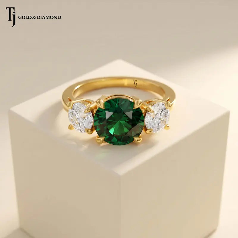 Front View of a round cut lab-created emerald trilogy engagement ring in 18kt yellow gold with round brilliant lab-grown diamond side stones.