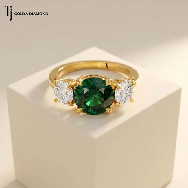 Front View of a round cut lab-created emerald trilogy engagement ring in 18kt yellow gold with round brilliant lab-grown diamond side stones.