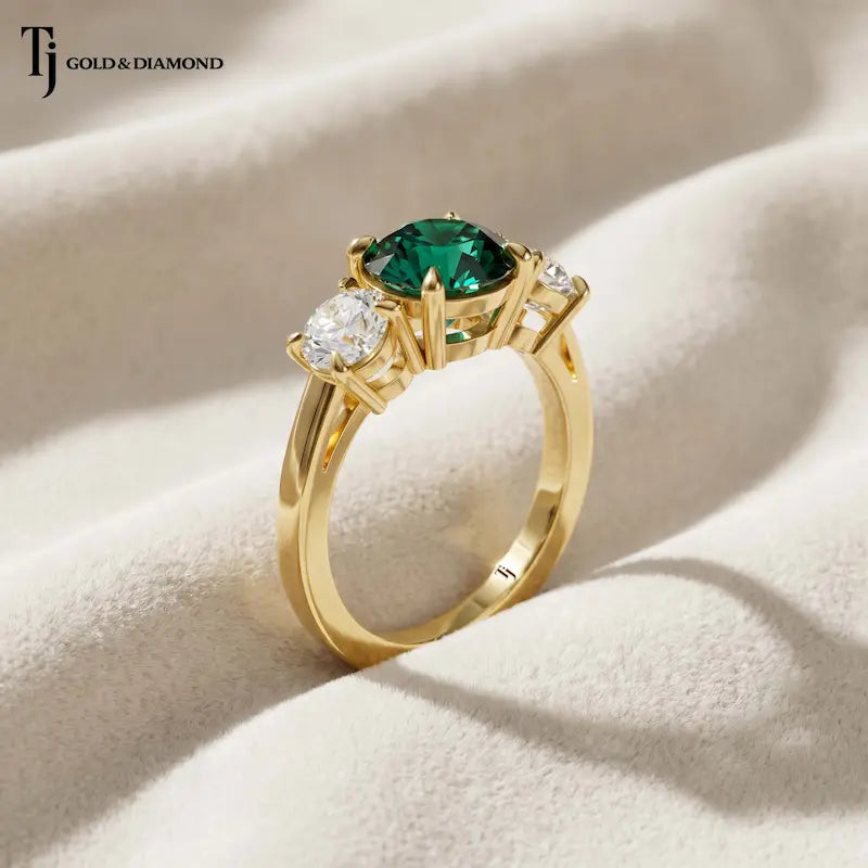 Side Profile View of a round cut lab-created emerald trilogy engagement ring in 18kt yellow gold with round brilliant lab-grown diamond side stones.