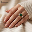 Round cut lab-created emerald trilogy engagement ring in 18kt yellow gold with round brilliant lab-grown diamond side stones, worn on hand.