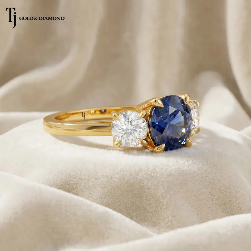 Angled close-up of a Round Cut Lab-Created Blue Sapphire & Lab-Grown Diamond Trilogy Ring in polished 18kt yellow gold.