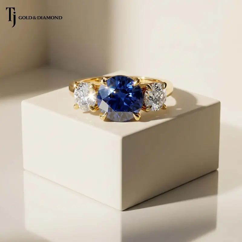 Round Cut Lab-Created Blue Sapphire & Lab-Grown Diamond Trilogy Ring in 18kt yellow gold featuring a royal blue round sapphire with round brilliant lab-grown diamond side stones.
