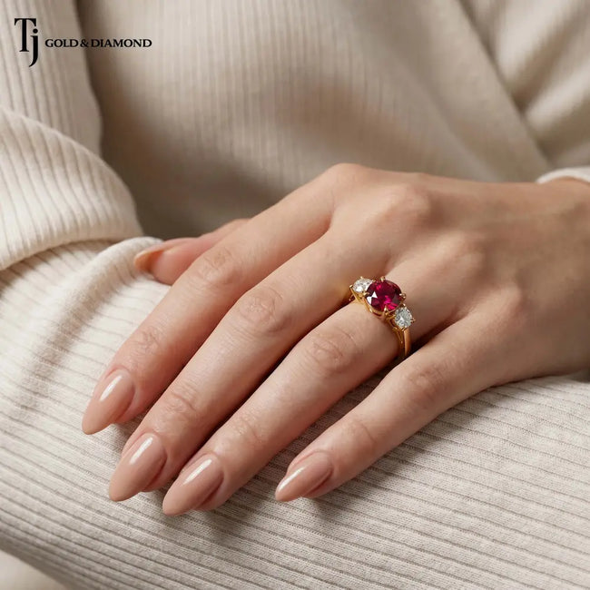 Hand wearing a round brilliant lab-created ruby trilogy engagement ring in 18kt yellow gold with round brilliant lab-grown diamond side stones.
