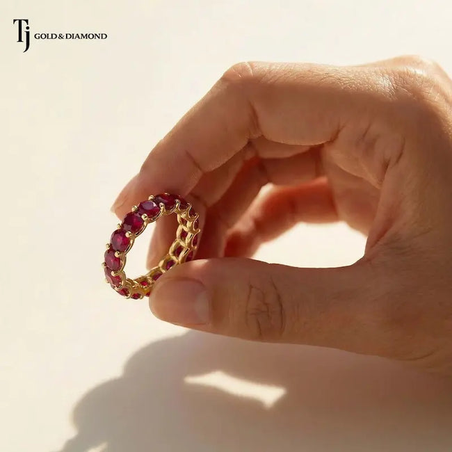 Created ruby full eternity ring in 18kt yellow gold held in hand with round brilliant lab-created rubies.