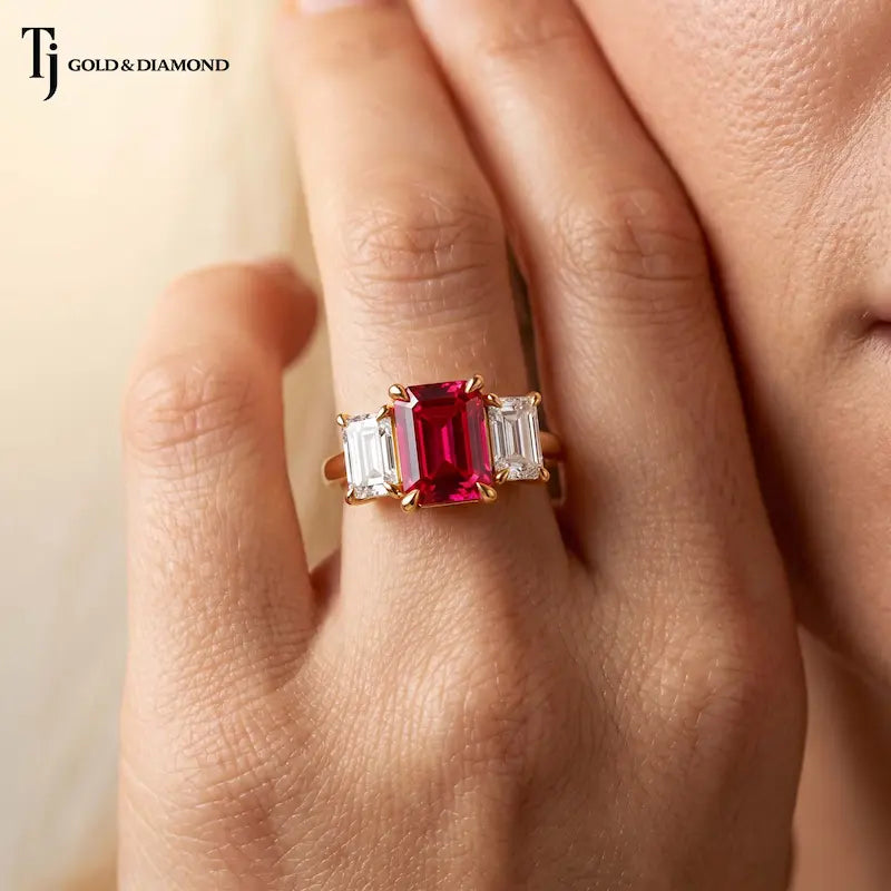 Close Up view of Emerald cut lab-created ruby trilogy engagement ring in 18kt yellow gold with emerald cut lab-grown diamond side stones worn on hand