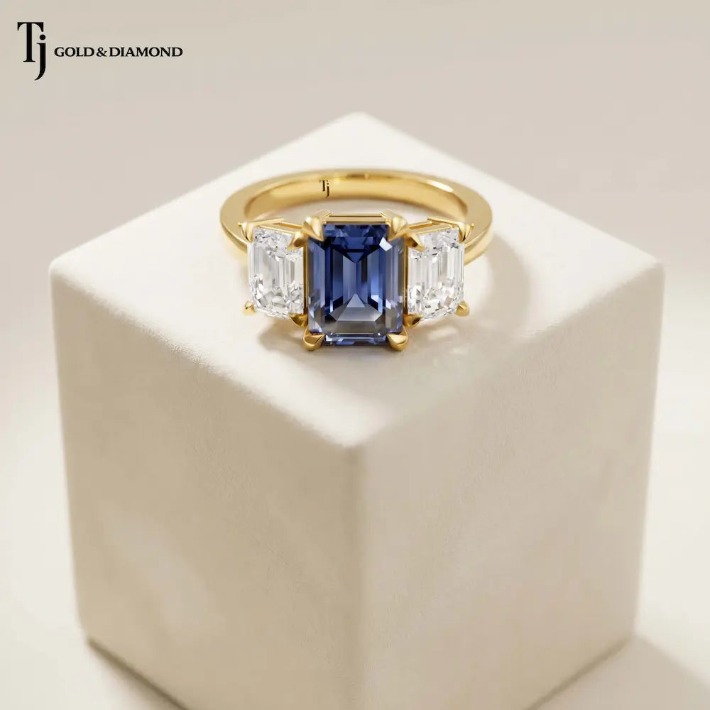 Created emerald cut sapphire and diamond trilogy ring in 18kt yellow gold featuring a vibrant blue lab-created sapphire with emerald cut lab-grown diamond side stones