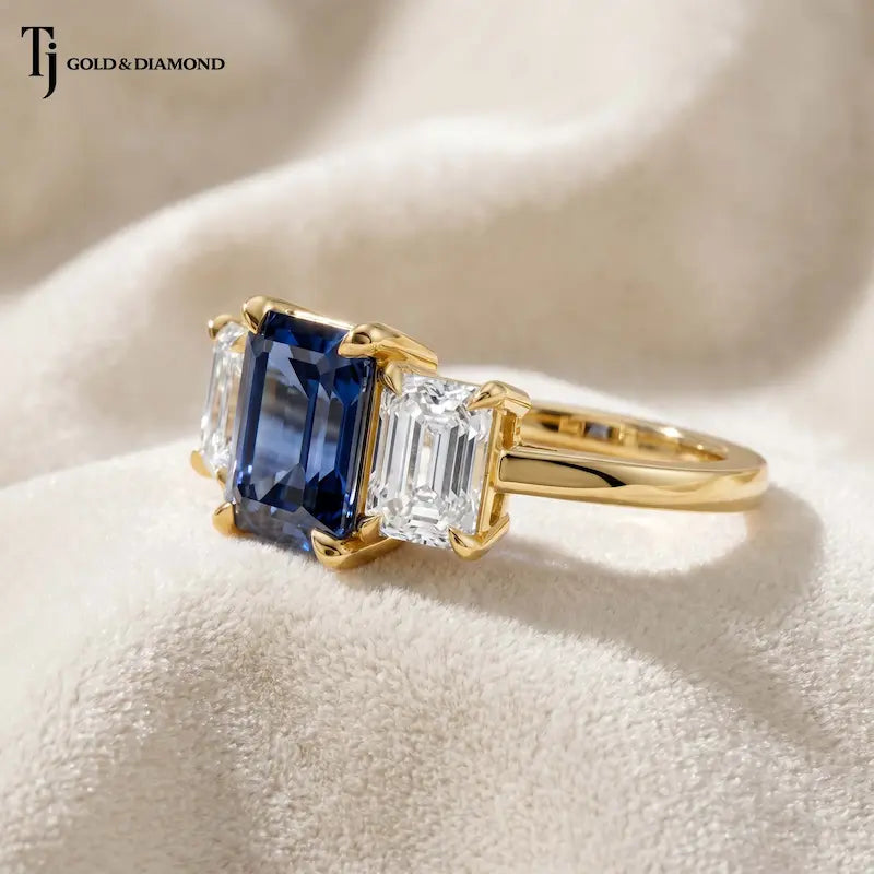 Angled view of a created emerald cut sapphire trilogy ring in 18kt yellow gold with emerald cut lab-grown diamond side stones and polished yellow gold band.