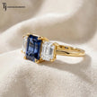 Angled view of a created emerald cut sapphire trilogy ring in 18kt yellow gold with emerald cut lab-grown diamond side stones and polished yellow gold band.