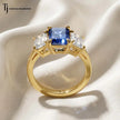 Side view of a created emerald cut sapphire trilogy ring in 18kt yellow gold displaying the handcrafted setting and emerald cut diamond side stones.