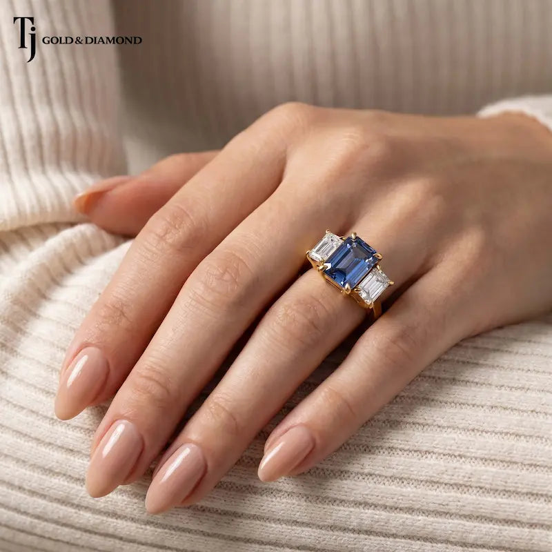 Created emerald cut sapphire and diamond trilogy ring worn on hand in 18kt yellow gold showcasing the elegant proportions and everyday wear.