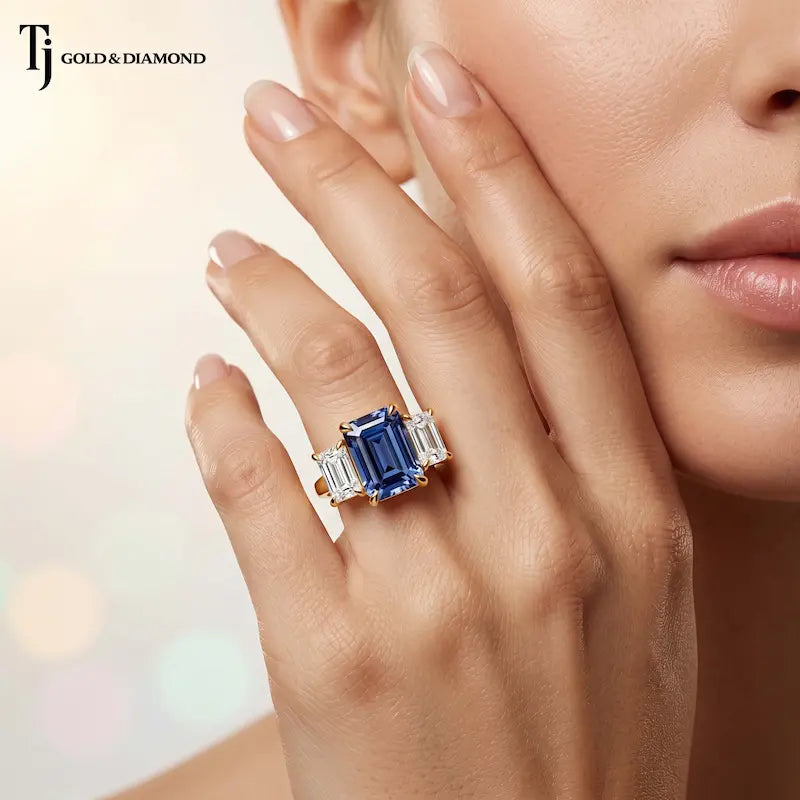 Close-up of a model wearing a created emerald cut sapphire and diamond trilogy ring in 18kt yellow gold with emerald cut lab-grown diamond accents.
