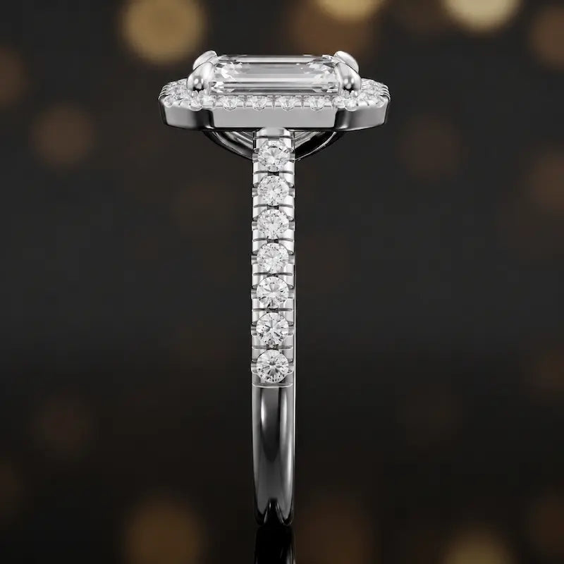 Side profile of an emerald cut halo lab-grown diamond engagement ring with diamond-set shoulders in 18kt white gold.